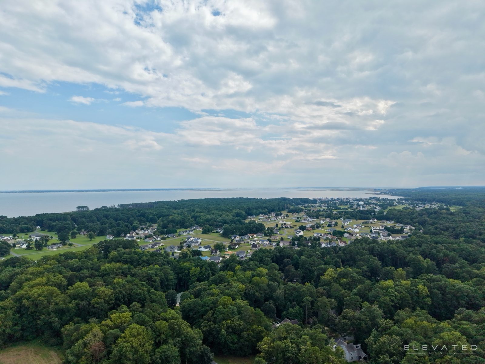 Neighborhood set in the woods beside a wide bay under a cloudy sky