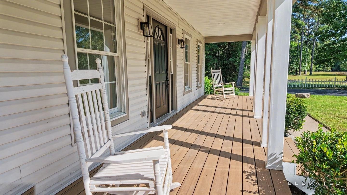 Covered front porch with white rocking chairs and a view of the lawn